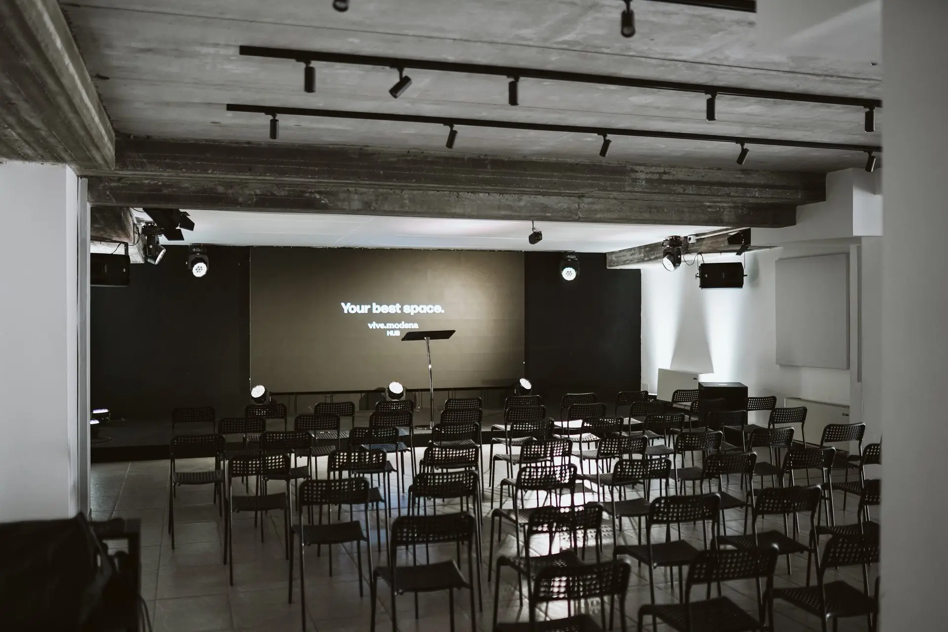 Sala conferenze con file di sedie nere davanti a uno schermo con la scritta "Your best space."