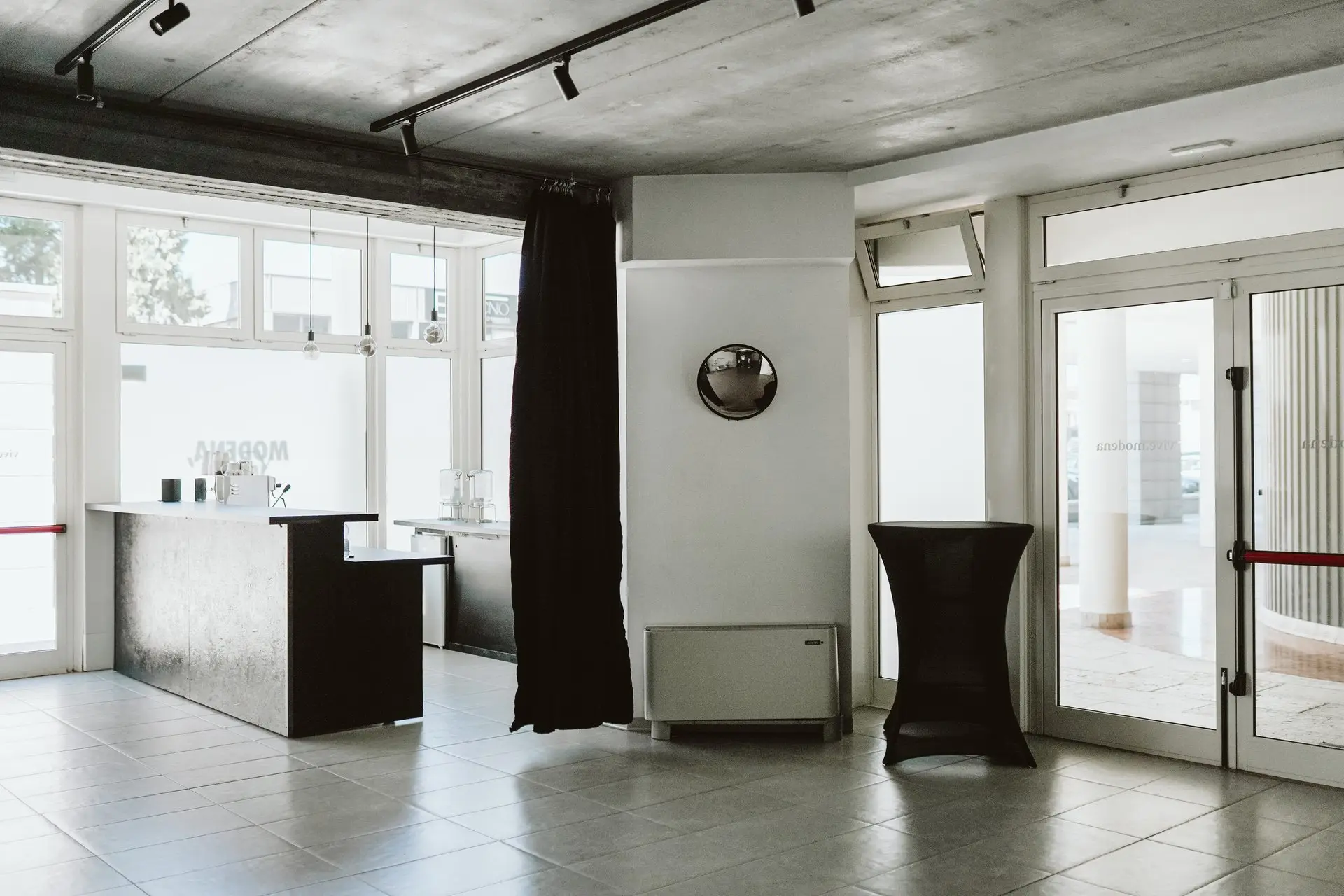 Spazio eventi moderno con bancone bar scuro, tavolo alto e grandi vetrate