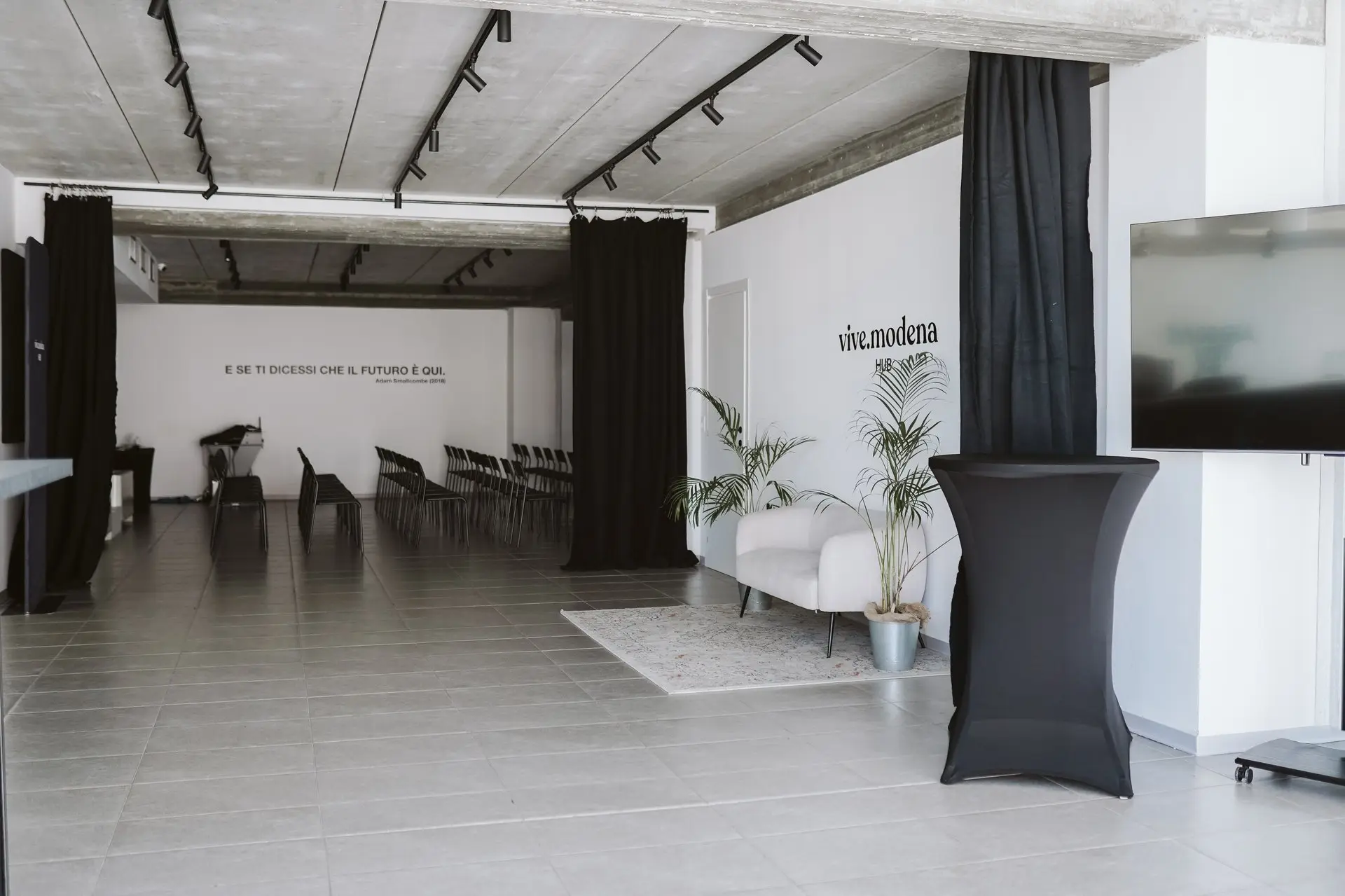 Spazio eventi moderno con pareti bianche, soffitto in cemento e tende nere