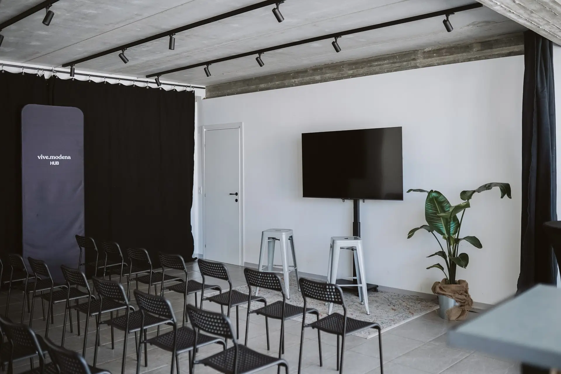 Sala presentazioni moderna con file di sedie nere, grande schermo e pianta