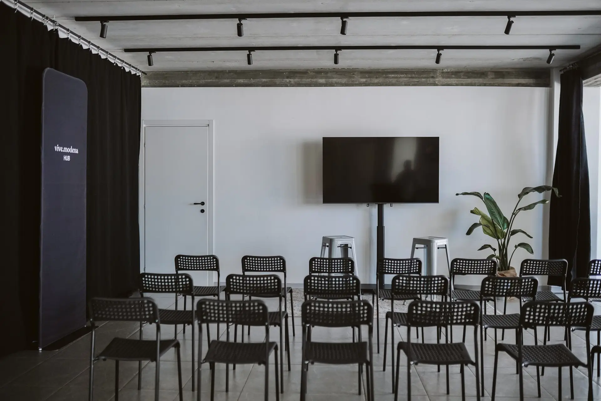 Sala conferenze moderna con sedie nere, grande schermo e pianta alta